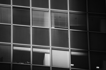The windows of a skyscraper office building creating an interesting abstract texture. Black and white architecture photo with sky reflection in windows.