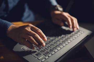 Businessman close up hand typing on laptop computer keyboard for 
working on woodern table in office. Man sitting wood table and using notebook texting message keyboard.
