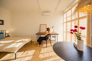 Interior of sunny studio apartment in beige tones with working place and woman spending leisure...
