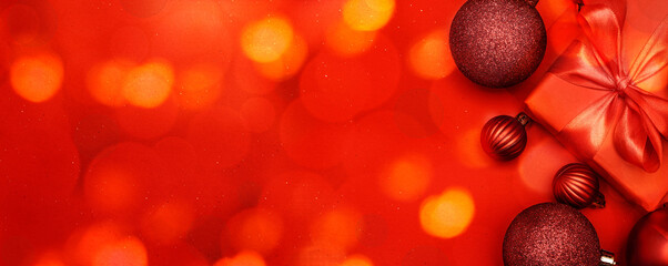   Christmas decorative composition with red shiny Christmas balls and gift on red background. Christmas or New Year concept. Christmas lights. Festive Christmas background with baubles and copy space.