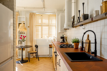 Stylish kitchen interior with open shelves, tiled table top, black sanitary and dining place behind at modern studio apartment