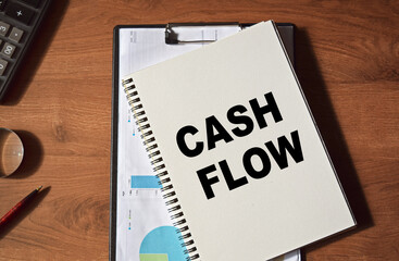 The inscription CASH FLOW written in a notebook, against the background of office supplies. Top view of the desktop. Business concept.