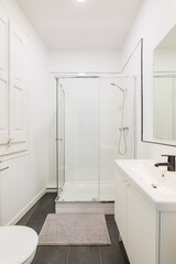 Modern white bathroom with shower cabin in renovated apartment.