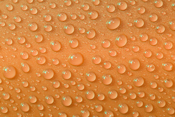 Close-up, orange, green, water droplets, on shiny, orange plastic surface, fresh, vibrant, glittering, filling the frame 