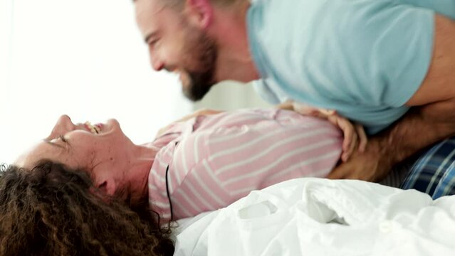 Happy couple, tickling and bedroom fun in the morning while playing, having fun and bonding in pyjamas while laughing and feeling joyful. Man and woman enjoying honeymoon in their England home