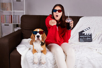 A young girl with her dog beagle in 3 d glasses watching a movie at home. A teenager is holding a...