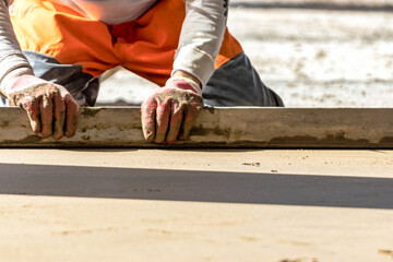 Close up of man builder placing screed rail on the floor covered with sand-cement mix at...