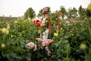 Portrait of a woman with lots of freshly picked up colorful dahlias and lush amaranth flower on...