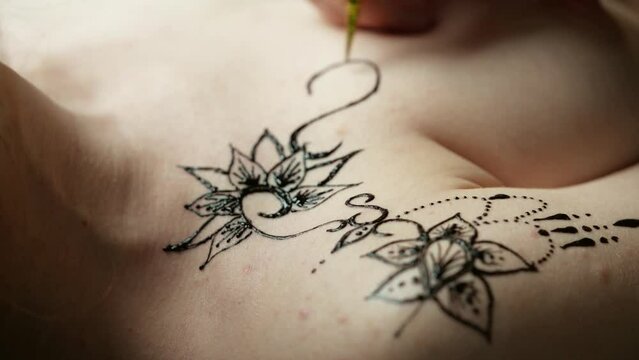 Artist applying henna tattoo on bare woman chest