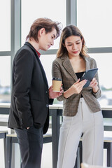 Millennial Asian successful professional female businesswoman in formal suit standing smiling showing data information on touchscreen tablet computer to male businessman colleague in company office