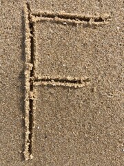 On the beach in the sand is carved the letter F