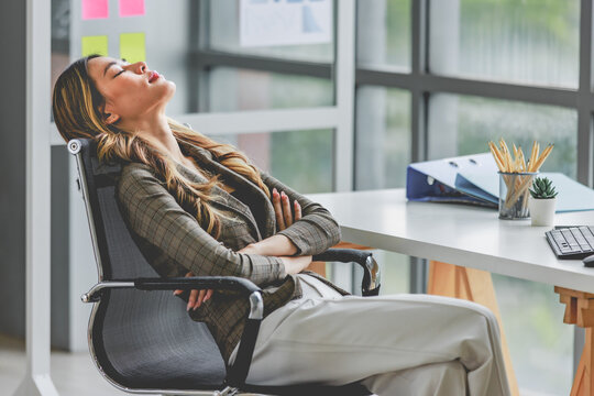 Millennial Asian tired exhausted female businesswoman employee in formal business suit sitting crossed arms close eyes sleeping napping take break on chair at workstation desk in company office