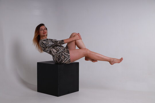 Woman with beautiful legs sitting on a black cube on grey background