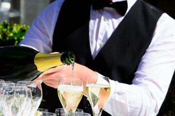 closeup of a champagne bottle pooring champagne into a champagne flute against a blurred waiter at...