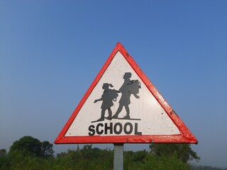 School sign plate in the roadside. Triangular school ahead sign plate near the road. Drive slow sign. School crossing sign in India. 
