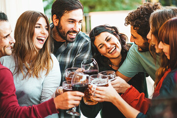 Cheerful millennial friends celebrating in the afternoon by clinking and toasting wine and beers...