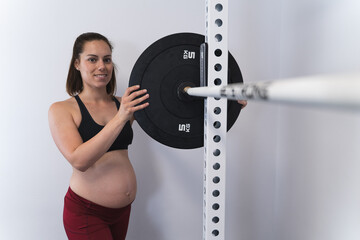 Pregnant woman placing weights on a barbell in a squat rack in a home gym