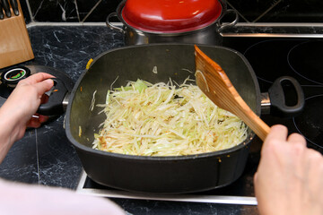 Young green cabbage is stewed in a frying pan at home in the kitchen.