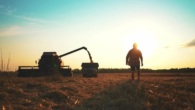 Silhouette one male farmers walking in a wheat field against sunset. Alone farmer stand in a field on the background of agricultural machinery. Agronomist plans harvest. Farmers concept.