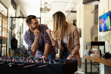Fototapeta premium Colleagues having fun at work. Businessman and businesswoman playing table soccer.