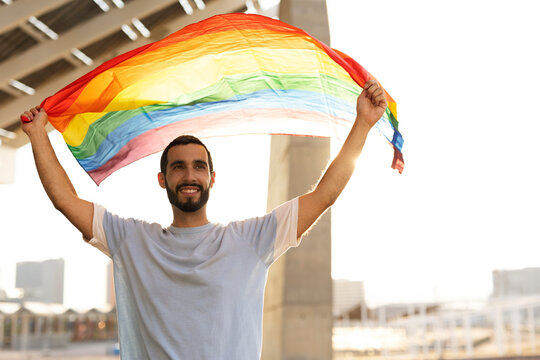 Happy gay man having fun holding rainbow flag symbol of LGBT community..