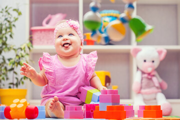 Fototapeta na wymiar baby girl playing with colourful building blocks at home or kindergarten