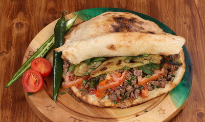 Roll stuffed with shish kebab with tomatoes, herbs, ketchup and amyonnaise on a wooden table