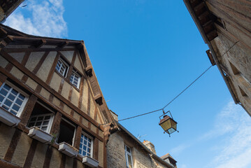Traditional homes with lattice structure in the historical centre of Dinan, Brittany, France. Ancient lamp is hanging on the street. Blue sky on the background.