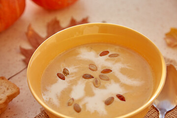 Healthy autumn pumpkin traditional french cream-soup with plant-based cream and seeds among autumn oak leaves