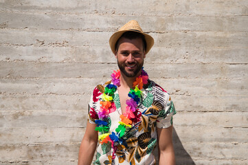 Handsome young man wearing a shirt with Hawaiian flowers, a hat and a necklace with coloured...