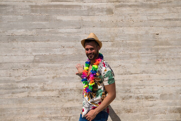 Handsome young man wearing a shirt with Hawaiian flowers, a hat and a necklace with coloured...