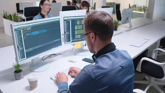 Close-up of male programmer coding on computer screen in office with many people. Man coding html code and programming on monitor creating a website. Web development, developer job