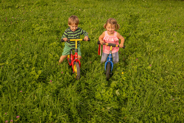 Little girl and boy having fun riding a bike in the grass