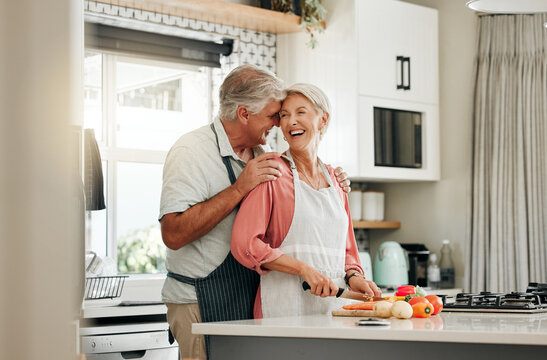 Senior couple in kitchen, cooking healthy food together and happy in retirement lifestyle. Elderly woman chopping vegetables with apron, old white man hug wife in home and love nutrition dinner meal