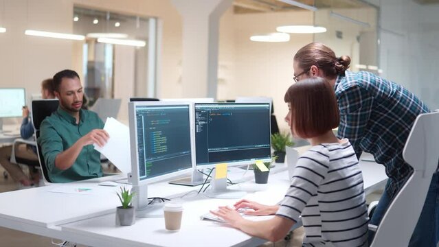Group of young IT programmers working in data center control room and discussing project. Male and female professionals coding on code language and speaking indoor. Workflow. People work in office