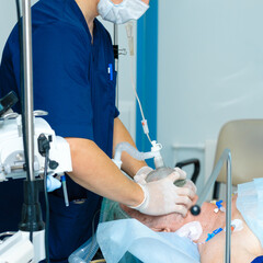 The doctor applies an oxygen mask to the face of an elderly man. Preparing a patient for surgery in...