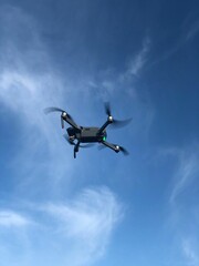 Vertical shot of a flying drone under blue sky with windy clouds