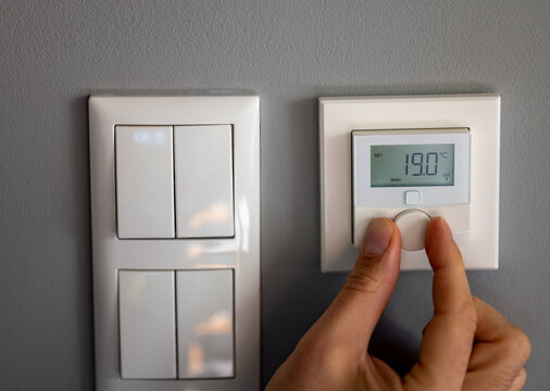 Hand turns down the temperature to 19 degrees Celsius on a electronic thermostat. Symbol for saving energy.