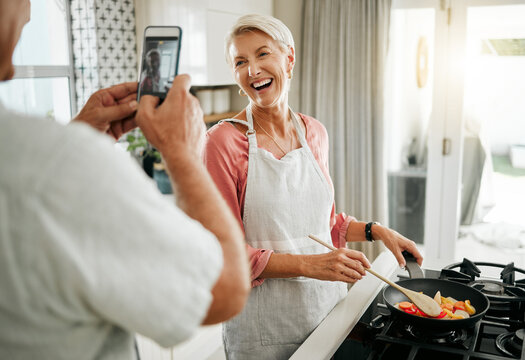Phone, man and woman taking a picture and cooking healthy food for dinner in a kitchen in a happy home. Smile, social media and elderly couple love having fun, memories and enjoying quality time