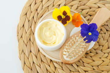 Fototapeta na wymiar Yellow hair mask (banana face cream, shea butter mask, mango body butter) in a small white jar and wooden hair brush. Natural skin and hair care treatment concept. Top view, copy space.