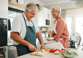 A happy senior couple, cooking healthy food in kitchen and drinking champaign as they enjoy...