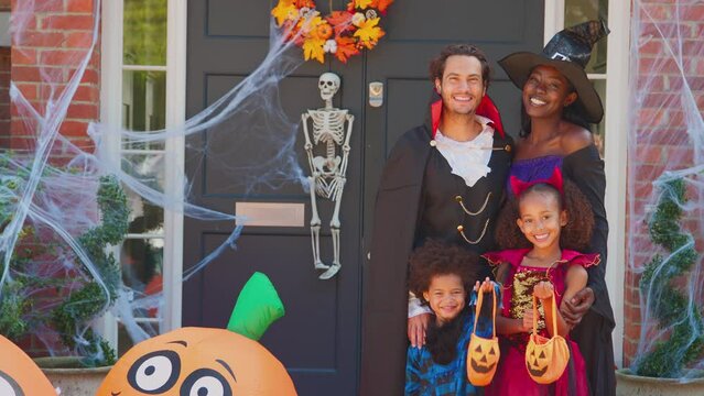 Family dressed in Halloween costumes outside house for trick or treat smiling at camera - shot in slow motion
