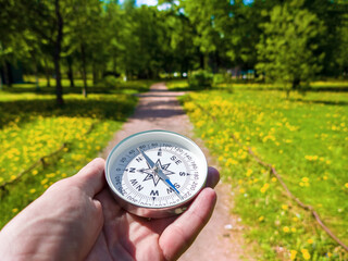 A compass in person's hand in park with flowers. Orient yourself in current situation (urban...