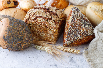 Fresh rye wheat loaf bread, various buns with seeds grains and ears closeup  on rustic table.