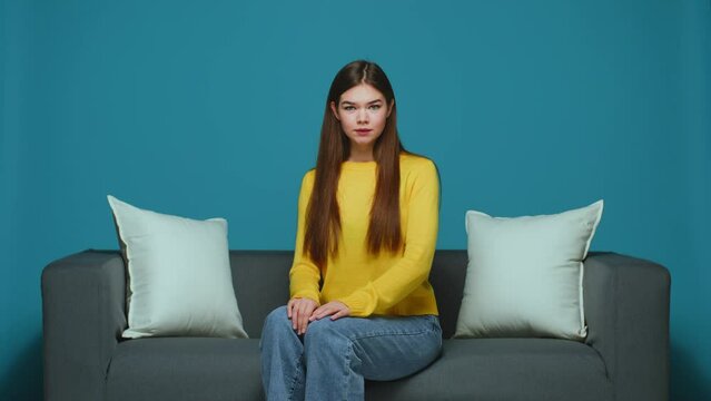 Displeased forgetful young caucasian girl makes facepalm gesture sitting on couch. Mistake, bad memory, shame emotion