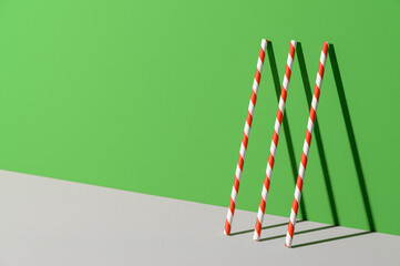 Eco friendly stripped paper straws stand leaning against the color wall. Ecology, recycling concept. Minimal geometric scene with copy space.