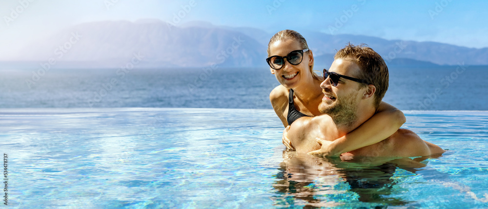 Wall mural happy couple in love having fun together in infinity swimming pool with sea view at adult resort. ro