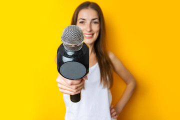 Smiling young woman holding a microphone, interviewing on a yellow background. Reporter or...