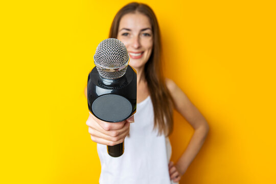 Smiling young woman holding a microphone, interviewing on a yellow background. Reporter or journalist concept