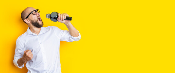 Singing young man with closed eyes with a microphone on a yellow background. Banner